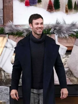 Dominick Whelton smiling in a wide-lapel black trench coat and ribbed turtleneck sweater with Christmas decor