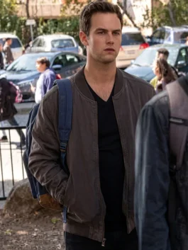 Brandon Flynn as Justin Foley wearing a dark grey bomber jacket, black v-neck t-shirt, and carrying a blue backpack