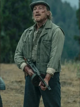 Jerome Flynn as Banner Creighton in a grey wool vest and flat cap, holding a Thompson submachine gun outdoors