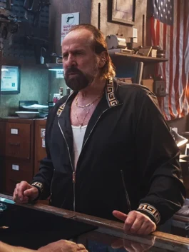 Peter Stormare as Troy in a black track jacket with gold Greek key patterns on the collar and cuffs, wearing gold chains