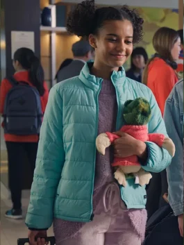 A smiling young woman with hair buns wearing a light blue puffer jacket while holding a stuffed frog toy