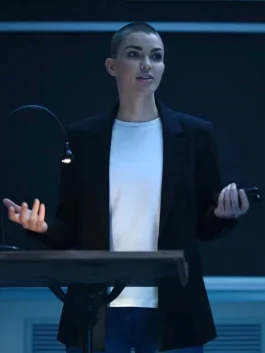 Ruby Rose as Parker with a buzzed haircut speaking at a podium in a sharp black blazer and white t-shirt