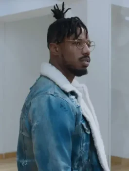 Profile view of Killmonger wearing the iconic distressed denim jacket with white shearling collar and gold-rimmed glasses.
