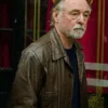 Actor Ron Cook with a grey beard looking sideways while wearing a distressed brown leather jacket with a collar