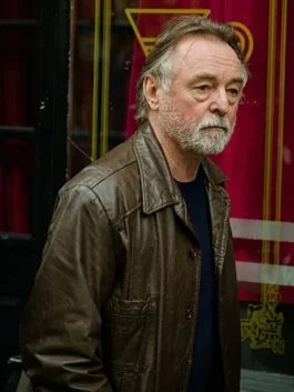 Actor Ron Cook with a grey beard looking sideways while wearing a distressed brown leather jacket with a collar