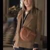 Jennifer Aniston wearing The Morning Show Alex Levy Camel Coat in a chic indoor look, styled with a brown shoulder bag and black outfit for a modern fashion vibe.