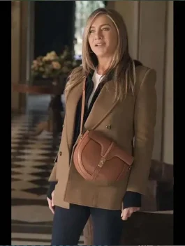 Jennifer Aniston wearing The Morning Show Alex Levy Camel Coat in a chic indoor look, styled with a brown shoulder bag and black outfit for a modern fashion vibe.