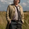Full-length shot of Gary Oldman portraying Jackson Lamb in an outdoor field setting. He is wearing his iconic Jackson Lamb beige trench coat and dark trousers, emphasizing the Gary Oldman Jackson Lamb coat from the spy series.