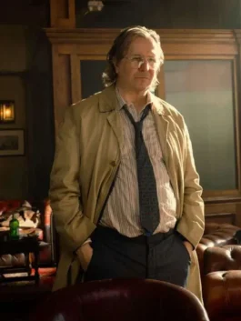 Gary Oldman as Jackson Lamb indoors wearing his signature unbuttoned beige trench coat over a striped shirt and dark tie, showcasing the Slow Horses Gary Oldman outfit and Jackson Lamb style coat.