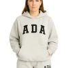 Front view of a woman in a light grey melange oversized hoodie with "ADA" printed in black collegiate lettering.