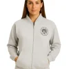 Front view of a woman in a light grey zip-up bomber jacket with a circular "Coast Club" logo on the chest.