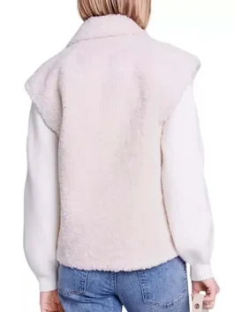 Back view of a cream sherpa vest with structured shoulders, worn over a white sweater with ribbed puff sleeves.