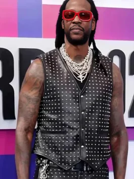 Rapper 2 Chainz on the red carpet wearing a black leather studded vest, layered chains, and red-framed sunglasses