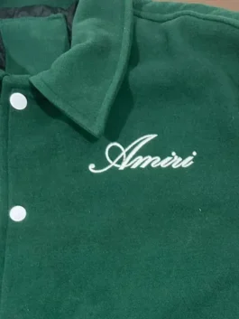 Close-up of the chest detail on the green Amiri bomber jacket, showing the white embroidered 