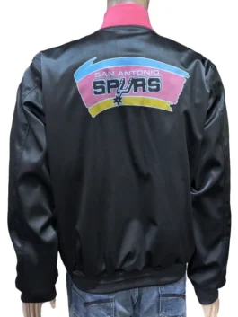 Back view of a black satin San Antonio Spurs pregame jacket featuring the vintage pink, orange, and teal logo and NBA Spurs warm up jacket style.