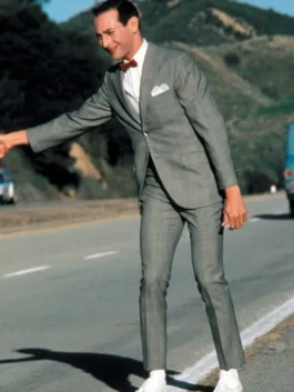 Peewee Herman wearing his classic grey peewee herman suit with a red bow tie and white shoes while standing on the roadside.