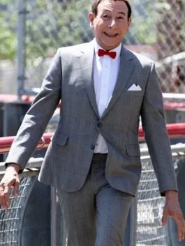 Pee Wee Herman walking outdoors in his classic grey pee wee herman suit with a red bow tie and white shirt.