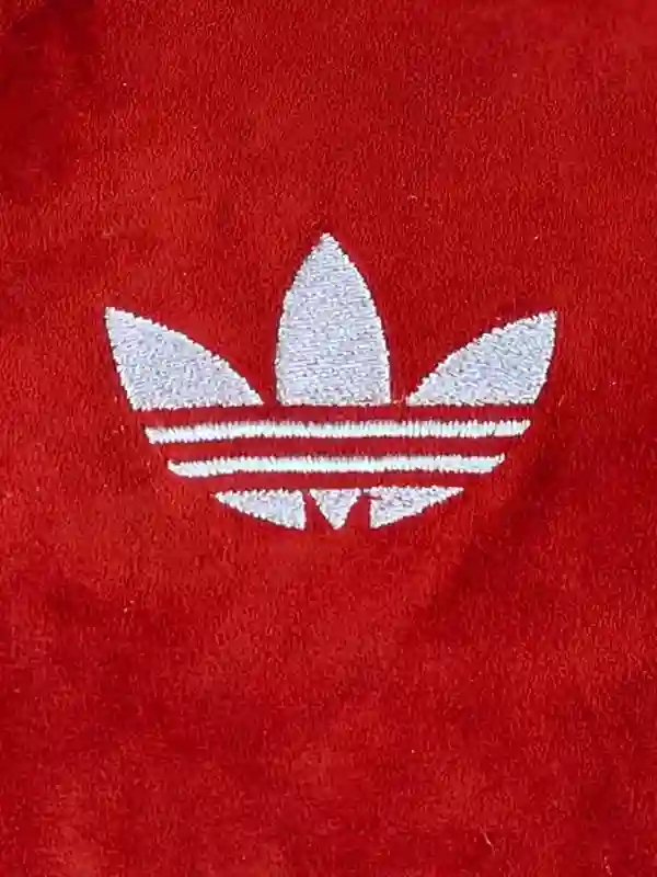 Detailed image of the red Adidas jacket showing the white Trefoil logo on the chest and contrasting sleeve stripes.