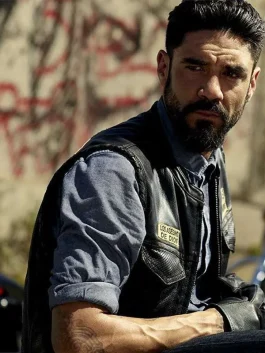 Clayton Cardenas wearing the Mayans M.C Angel Reyes Leather Vest with "Los Asesinos de Dios" patch in a close-up scene.