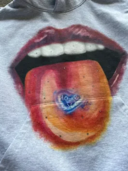 Detailed view of homesick apparel showing a tongue with a blue heart. This homesick x2c hoodie design highlights unique homesick clothing style.