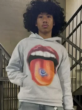 A person wearing a grey homesick hoodie featuring a large graphic of a mouth with red lips and a tongue holding a blue heart.