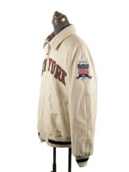 Left side profile view of the cream-colored Kith and Avirex New York Knicks leather jacket, highlighting the American flag Avirex patch on the sleeve.