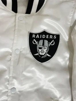 Close-up shot of the front chest pocket on a white Raiders jacket featuring the embroidered Raiders shield logo patch.