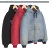 Three Supreme Reflective Arc Hooded Work Jackets hanging on wooden hangers in black, red, and light blue denim colors with embroidered Supreme logo across the chest