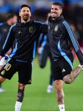 Lionel Messi and Rodrigo De Paul stretching, both wearing the Messi Argentina football hoodie, black with blue accents, ideal for supporters of Argentina's last home game or a Messi Argentina match day hoodie.