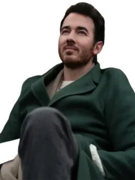 Kevin Jonas standing in a dark green coat that is zipped halfway up, over a dark shirt, looking straight ahead.