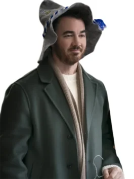 Kevin Jonas sitting indoors and looking contemplative, wearing a dark green coat unzipped over a collared shirt, with his hands clasped in front of him.
