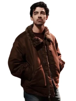 Joe Jonas looking straight ahead in a dark brown puffer-style jacket with a prominent brown shearling collar. He's wearing a dark undershirt and has his hands tucked into the jacket pockets.