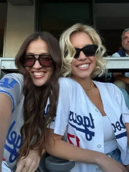 Selfie of Sydney Sweeney and a friend smiling while seated at a baseball game. Sydney Sweeney is wearing a white LA Dodgers Sydney Sweeney jersey with the number '17' visible, demonstrating her Sydney Sweeney Dodgers fan style and Sydney Sweeney white Dodgers jersey.