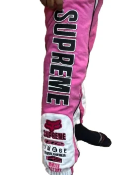 Close-up of the Supreme Fox Racing Sweatpant (FW25) in pink featuring vertical Supreme text and technical racing-style graphic patches.