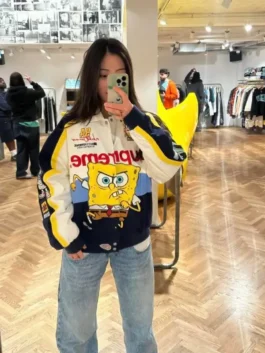 Full-body mirror selfie of a person wearing the white and navy Supreme SpongeBob SquarePants Cotton Racing Jacket with blue jeans, highlighting the vibrant spongebob racing jacket design.
