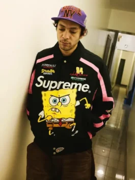 Close-up of a person wearing the black Supreme x Jeff Hamilton SpongeBob Jacket, a Supreme Jeff Hamilton Racing Jacket collaboration featuring the Spongebob graphic and a purple hat.