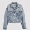 Front view of the light wash Beyoncé x Levi's Shrunken 90s Denim Trucker Jacket. The cropped jacket is embellished with an intricate, Western-inspired paisley pattern made of rhinestones across the shoulders, collar, front body, and sleeves. The jacket has a relaxed fit and traditional denim jacket pockets.