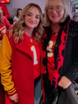 Alana Higman smiles while posing for a photo with an older blonde woman. Higman is wearing a red Kansas City Chiefs jersey with the number '1' and a red coat with yellow sleeves. The older woman is also wearing a Chiefs jersey.