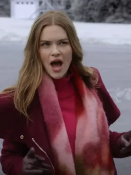 Close-up of Holland Roden looking surprised or excited, with her mouth open. She is outdoors in a winter setting, wearing a dark red or burgundy coat, a bright pink turtleneck, a fuzzy pink and red scarf, and dark gloves.