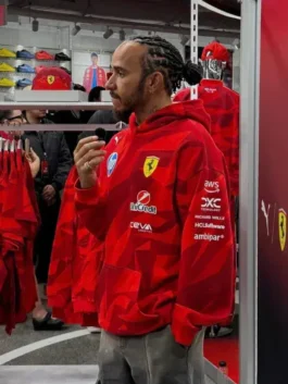 Side profile of the driver wearing the Lewis Hamilton 2025 Grand Prix hoodie, showing detailed sponsor logos on the sleeve including AWS and UniCredit inside a merchandise store.