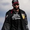 NFL player KhaDarel Hodge walking outdoors, wearing a black varsity jacket open to reveal a black t-shirt with the white script text "Historical Black Colleges & Universities." He is also wearing sunglasses, a cross necklace, and a "Dad Gang" baseball cap.