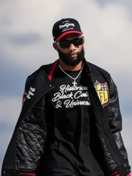 NFL player KhaDarel Hodge walking outdoors, wearing a black varsity jacket open to reveal a black t-shirt with the white script text 