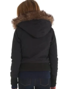 A rear view of a woman wearing the black Superdry Study Duffle Jacket. The image highlights the short, bomber-style length, the ribbed black waistband, and the wide Vegan fur trim around the hood.