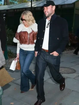 Sydney Sweeney walking outdoors in a casual outfit featuring a brown shearling short-sleeved leather jacket, alongside a man in a dark jacket.