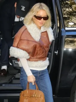 Sydney Sweeney stepping out, wearing a cropped brown shearling aviator jacket with a white long-sleeve top and blue jeans, holding a brown handbag.