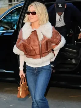 Sydney Sweeney exiting a car in a brown short sleeve shearling aviator jacket over a white top, paired with flared blue jeans and sunglasses.