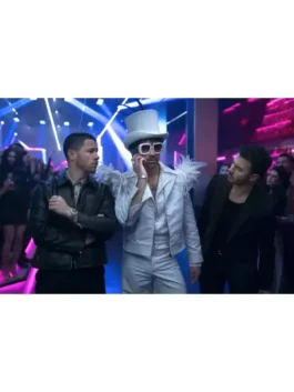Joe Jonas, dressed in an Elton John-inspired sparkling white suit with a matching top hat, white feather epaulets, and red-tinted sunglasses, stands in a brightly lit nightclub. He is talking on a cell phone. To his left, Nick Jonas wears a black leather jacket over a striped shirt. To his right, Kevin Jonas wears a black suit jacket over a dark shirt.