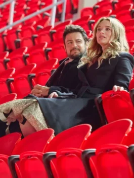 Two film actors stills from Holiday Touchdown: A Bills Love Story featuring actress Alana Higman: one shows her smiling in a dark coat inside a shop with football merchandise, and the other shows her in a dark wool coat seated next to a man in a stadium filled with red seats.