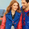 Holland Roden and Matthew Daddario pose together in front of a snowy stadium background. Roden, with long red hair, smiles while wearing a striking royal blue coat with red leather sleeves over a black Buffalo Bills t-shirt. Daddario smiles beside her, also wearing a blue and red jacket.