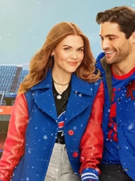 Holland Roden and Matthew Daddario pose together in front of a snowy stadium background. Roden, with long red hair, smiles while wearing a striking royal blue coat with red leather sleeves over a black Buffalo Bills t-shirt. Daddario smiles beside her, also wearing a blue and red jacket.